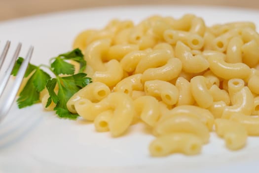 Boiled yellow pasta on a white plate with a fork. Close-up.
