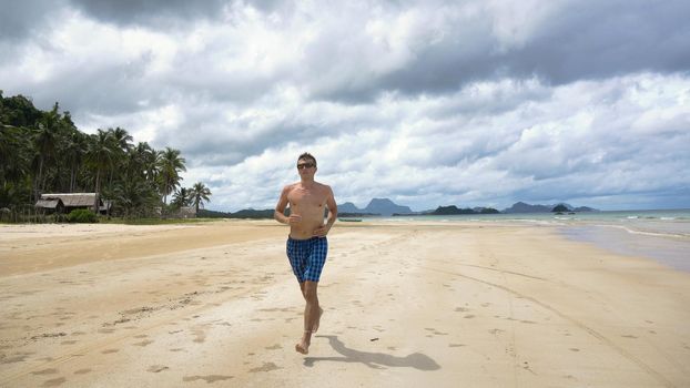 Man running along beach. Fitness sports runner man jogging on beach. Handsome young fit sporty male athlete running outside on beautiful beach training.