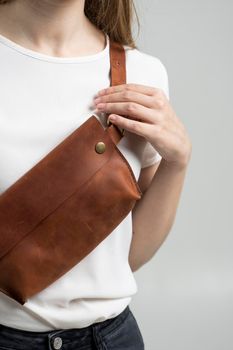 Girl in a white blouse with a leather brown handmade bag over her shoulder. Designer brown banana bag. Woman in a studio. Comfortable small bag for walking