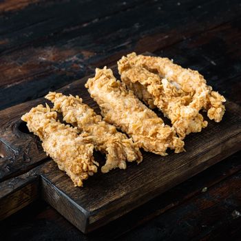 Fried crispy chicken stripes parts on old dark wooden table.