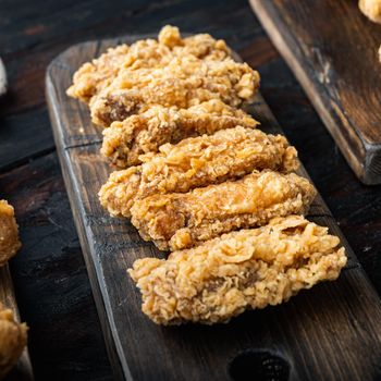 Spicy deep fried breaded chicken wings cuts on dark wooden background.