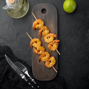 Grilled shrimp skewers. Seafood, shelfish. Shrimps Prawns skewers with herbs set, on wooden serving board, on black background, top view flat lay