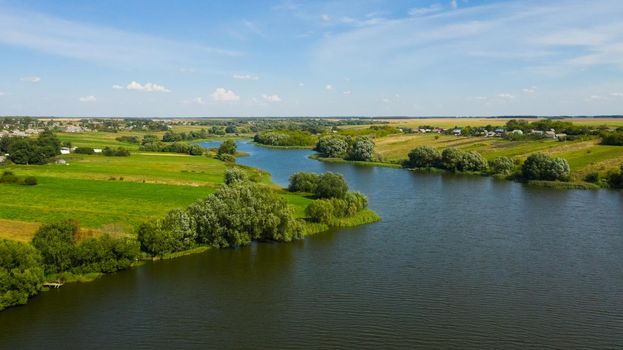 The river flows through the countryside surrounded by green meadows in the summer.