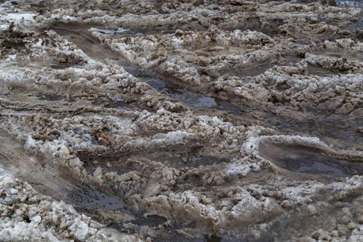 thick dirty wet snow layer with many car wheel tracks on winter street - full frame background with selective focus and blur