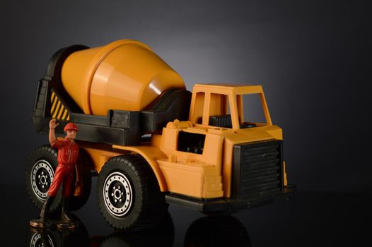 A toy cement mixer and a miniature working man waving over a dark gradient background.
