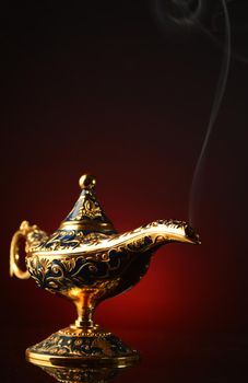 A vertical image of a brass magical Genie oil lamp with a smoke trail coming out of the spout.