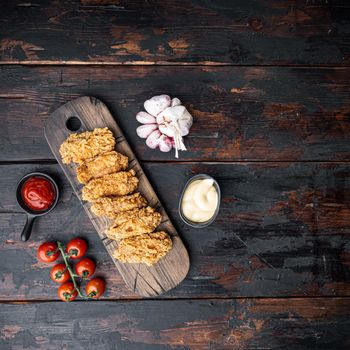 Spicy deep fried breaded chicken wings cuts on dark wooden background, flat lay, with space for text.