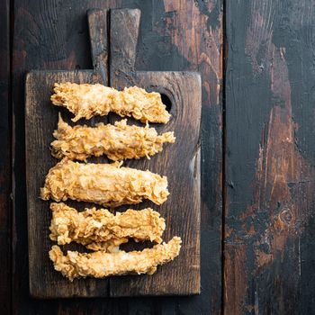 Chicken breaded breast fillet on dark wooden background, top view, with space for text.