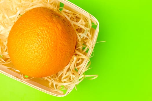 orange in a basket with shavings on a green background. High quality photo