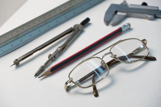 Glasses and drawing supplies are on the table in the school classroom. University academic subjects for geometry.Ruler, compass, pencil, caliper and glasses on a white background.