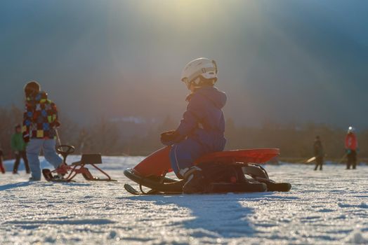 child comes down from the mountain riding a red sled in winter