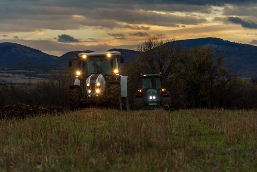 Farmer in tractor preparing land with cultivator at night