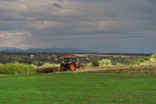 Farmer with tractor seeding crops at field in spring