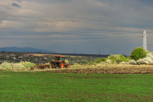 Farmer with tractor seeding crops at field in spring