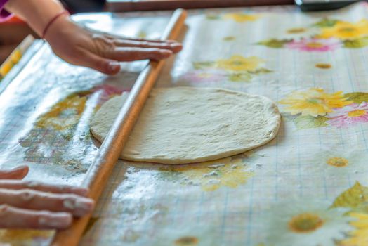 female hands rolling raw dough on white table at home