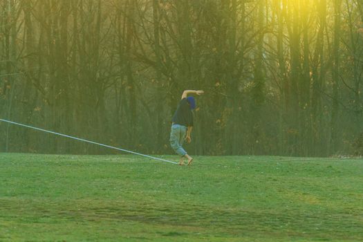 Handsome young man walking on slackline in the park at sunset
