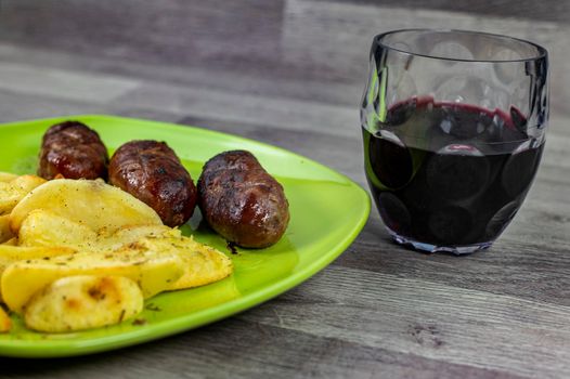plate sausages potatoes and glass of wine on wooden background