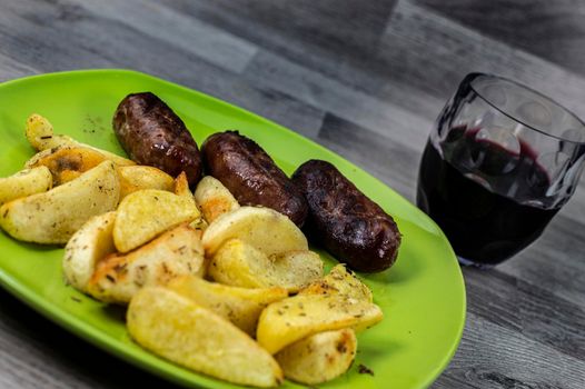 plate sausages potatoes and glass of wine on wooden background