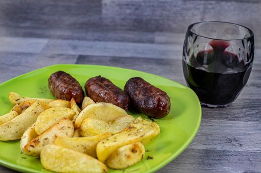 plate sausages potatoes and glass of wine on wooden background