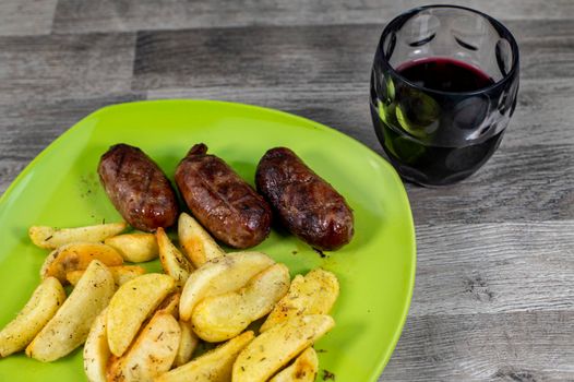 plate sausages potatoes and glass of wine on wooden background