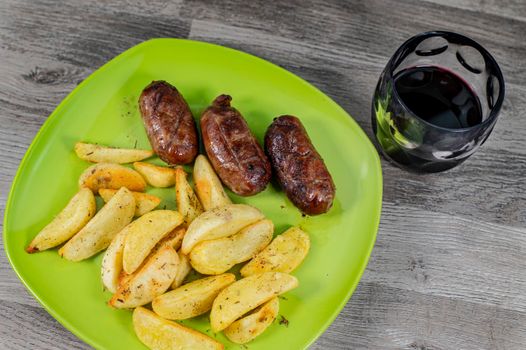 plate sausages potatoes and glass of wine on wooden background