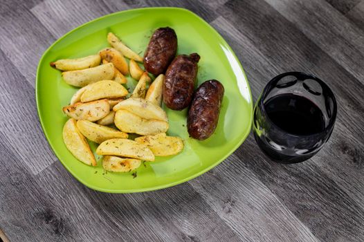 plate sausages potatoes and glass of wine on wooden background