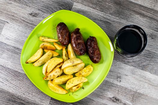 plate sausages potatoes and glass of wine on wooden background