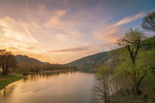 Sunset on the lake with forest with green grass in summer