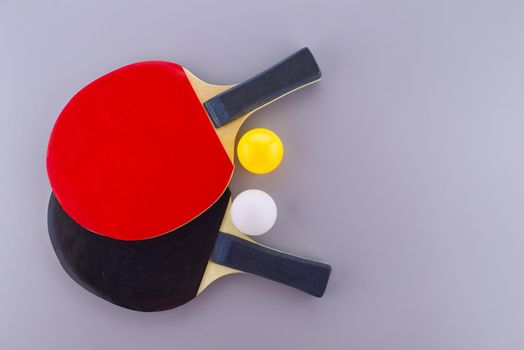 Red and black table tennis racks with a white and an yellow ping pong ball on grey background