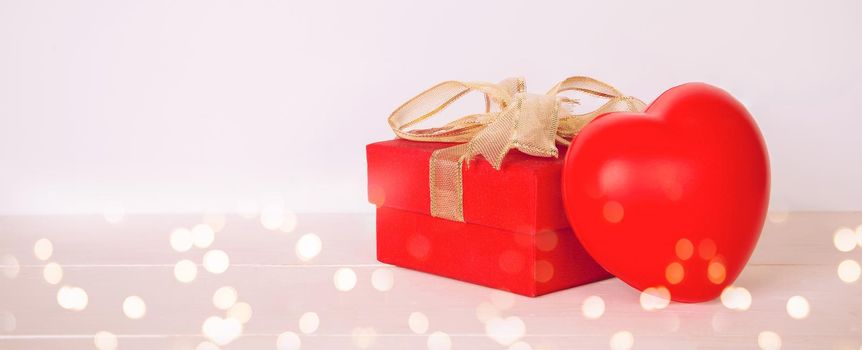 Red gift box and heart shape on wooden table with bokeh background, love and romance, presents in celebration and anniversary with surprise on desk, happy birthday, valentine day concept.