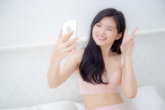 Beautiful young asian woman sexy in underwear talking a selfie on smartphone for social network in the bedroom, girl in lingerie relax with taking a picture on mobile phone on bed in the bedchamber.