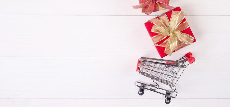 Cart of supermarket and gift box on wooden table, shopping online for presents in valentine day, trolley for sale commerce in holiday and vacation, copy space, celebration and anniversary concept.
