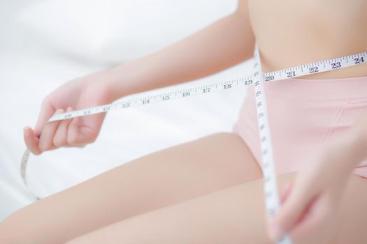 Beautiful young asian woman sexy body slim measuring abdomen for control weight loss in the room, beauty girl belly thin have cellulite with tape measure for diet, health and wellness concept.