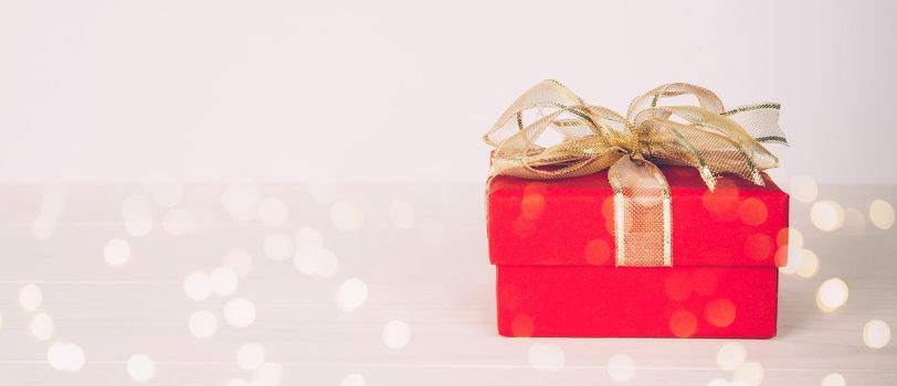 Red gift box on wooden table with bokeh background, love and romance, presents in celebration and anniversary with surprise on desk, happy birthday, copy space, nobody, valentine day concept.