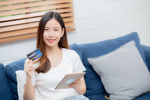 Young asian woman smiling holding credit card shopping online with tablet computer buying and payment, girl using debit card purchase or transaction of finance, lifestyle and e-commerce concept.