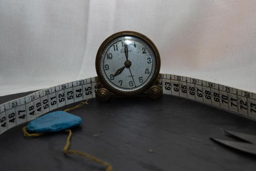 Clock surrounded by sewing utensils such as needle, thread and sewing tape measure.