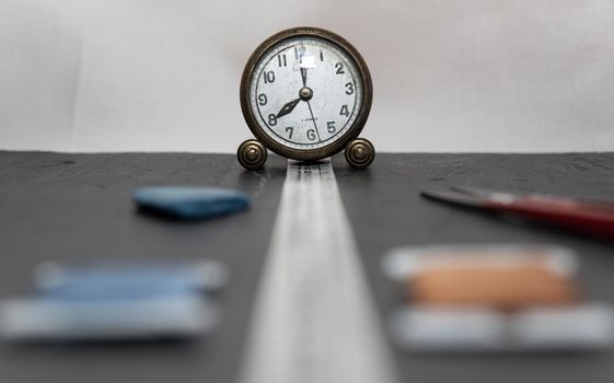 Clock surrounded by sewing utensils such as needle, thread and sewing tape measure.