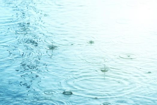 Raindrops creating concentric circles and droplets on a puddle water surface