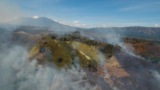 Aerial view forest fire on the slopes of hills and mountains. Forest and tropical jungle deforestation for human food farming and export. large flames from forest fire. Using fire to destroy natural habitat and causing large scale environmental damage in Asia. Jawa island, Indonesia.