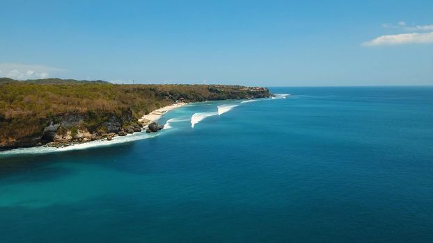 Aerial view of beautiful beach, hotels and tourists, Bali, Indonesia. Beach with rocky mountains and clear water of Indian ocean at sunny day. Seascape: ocean, sky, sea.