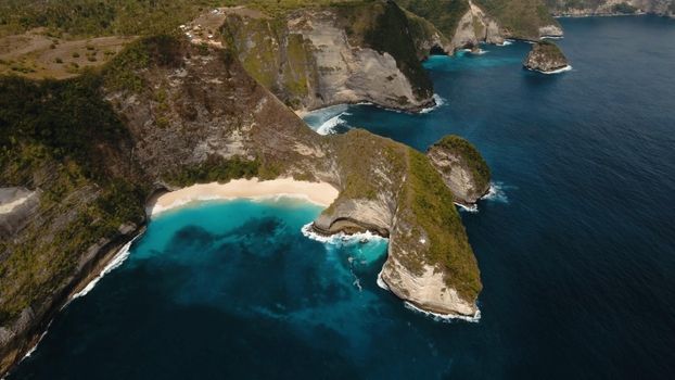 Wild tropical beach at the foot of the cliff. Tropical beach among rocky cliffs. Karang Dawa, Manta Bay or Kelingking Beach on Nusa Penida Island, Bali, Indonesia. Travel concept.