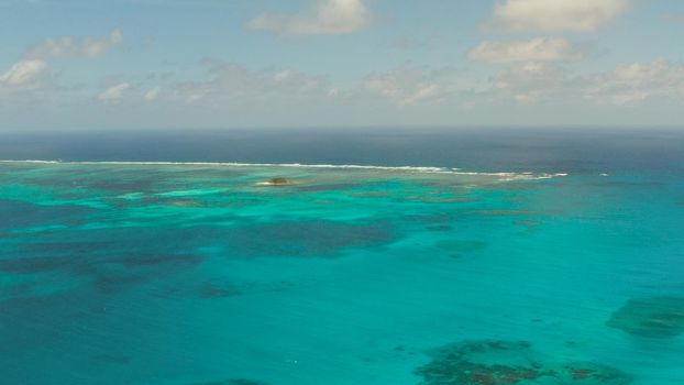 Top view of turquoise water of the atoll against the backdrop of the tropical island and sky with clouds. Travel concept.