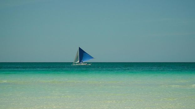 Sailing boat in crystal clear turquoise water, from above. Sailing yacht glides over the waves, Boracay, Philippines.