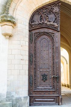 Light brown, antique wooden doors with carvings and patterns. Metal handles made of gold. A semicircular vault. Entrance to the house.