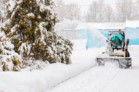 In winter the tractor clears the snow covered road throwing snow in the direction of the Christmas tree