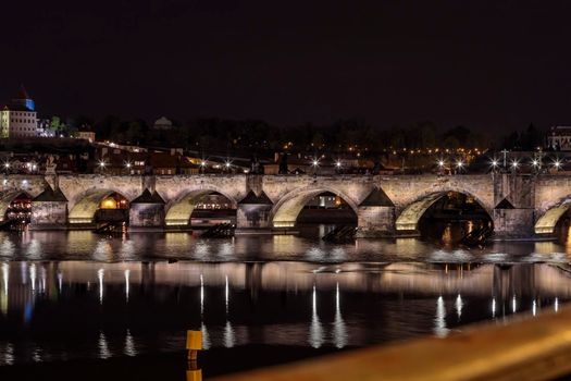 Charles Bridge in Prague in the evening with colorful lights from lanterns. In the river the reflection of the evening illuminations.