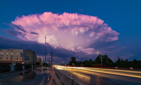 A large pink cloud in the form of a mushroom, in the evening after the rain. Glowing lights from the cars. Tracer beam. Tinting