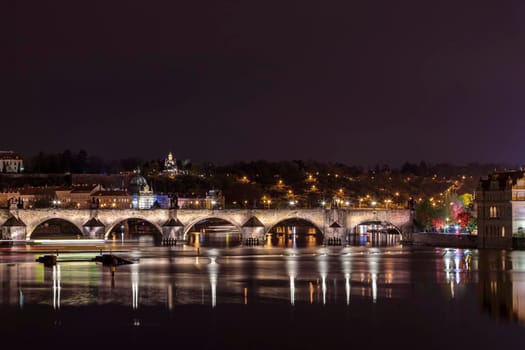 Charles Bridge in Prague in the evening with colorful lights from lanterns. In the river the reflection of the evening illuminations.