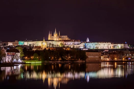 Charles Bridge in Prague in the evening with colorful lights from lanterns. The river reflects the evening illumination and old castles.