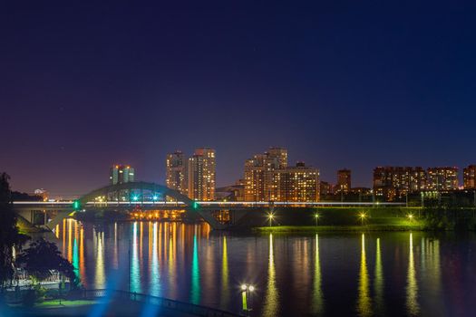 Night city in bright lights. Railway bridge over the river. Reflection of lanterns in the water.